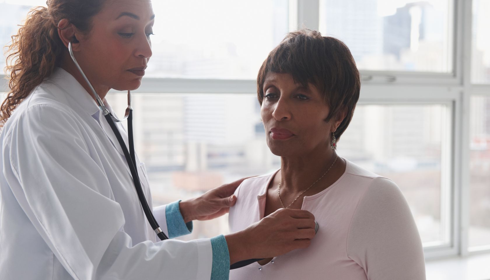 Doctor listening to heartbeat of patient near window