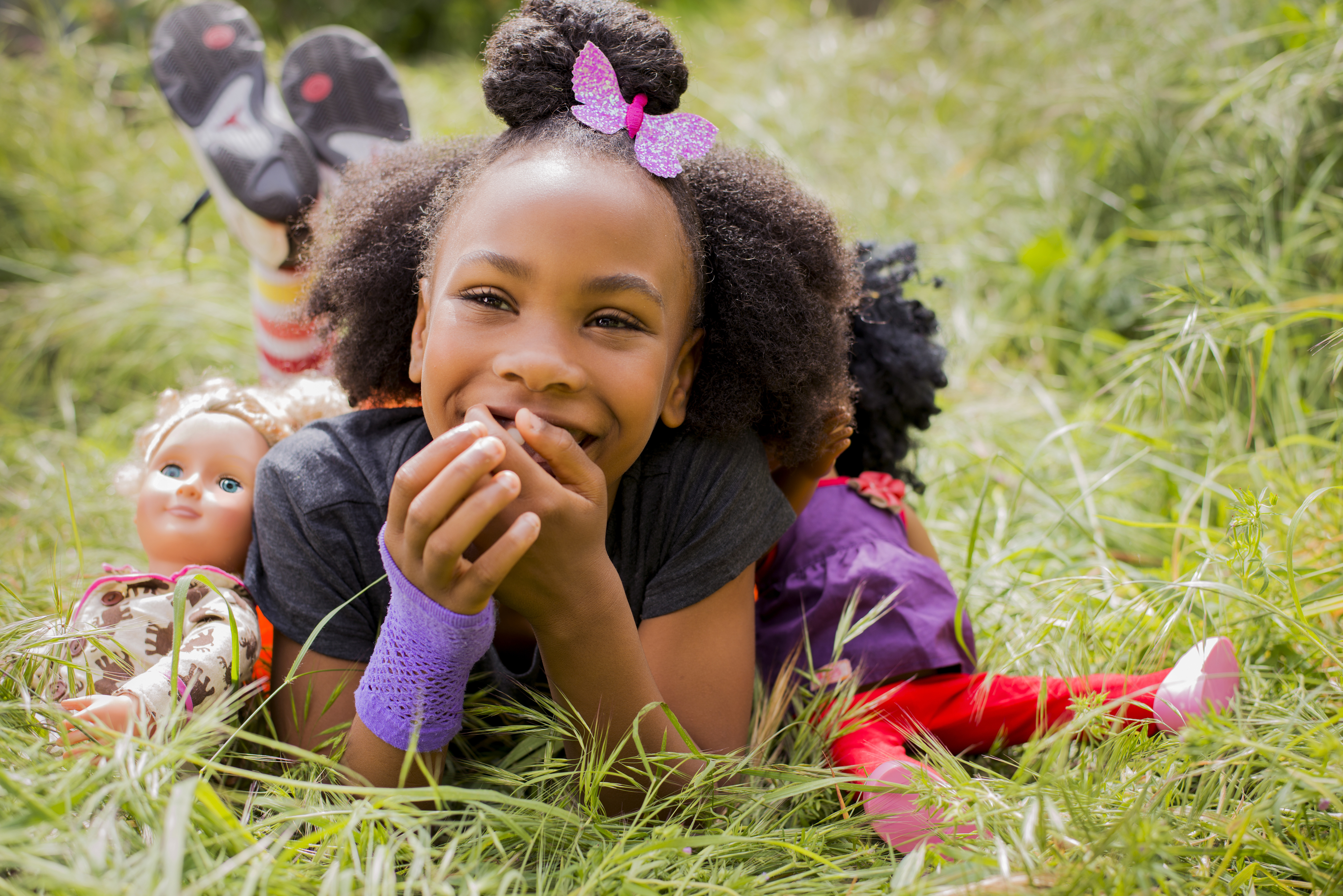 Black girl playing with dolls in tall grass