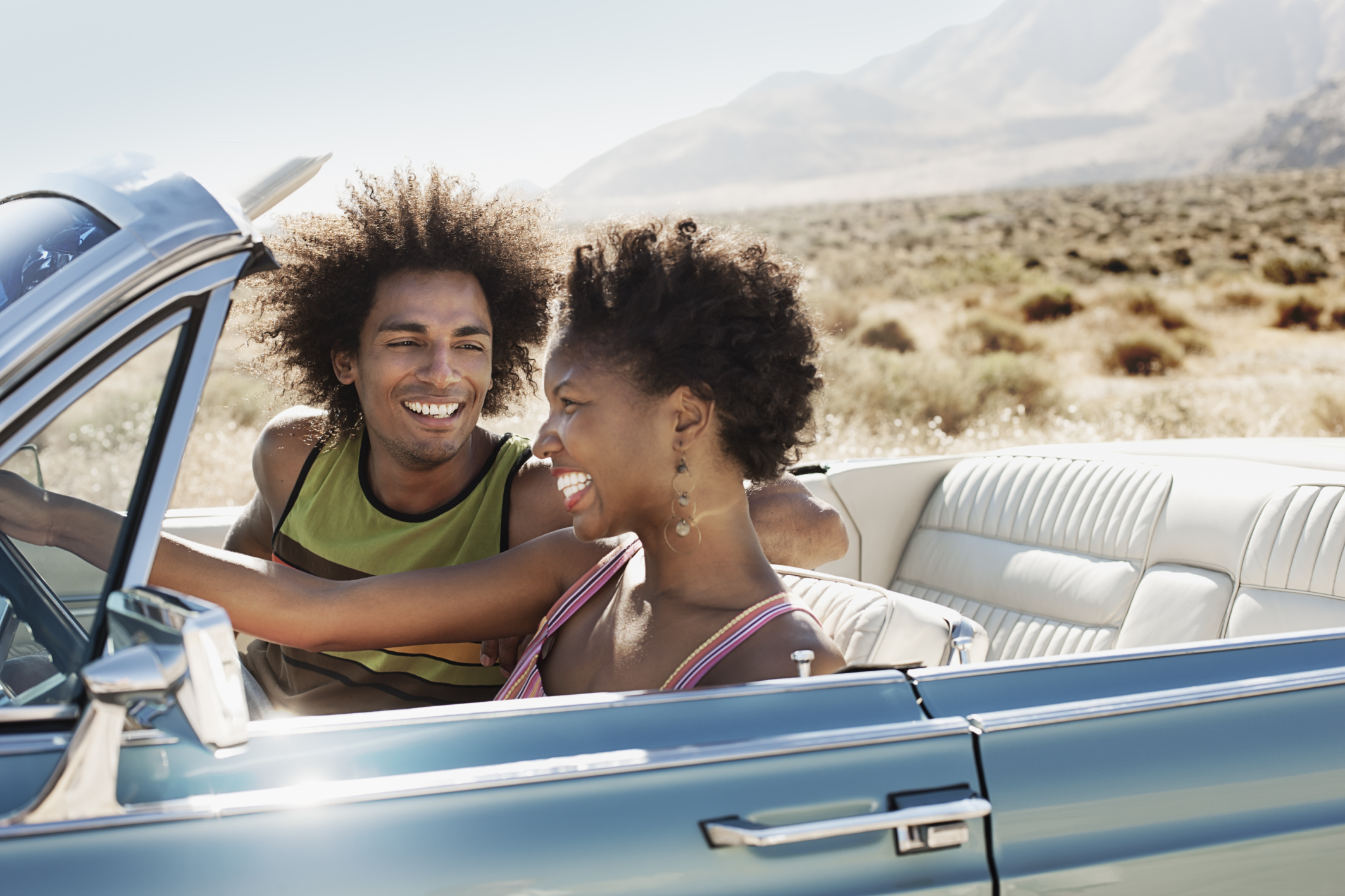 A young couple, man and woman in a pale blue convertible on the open road