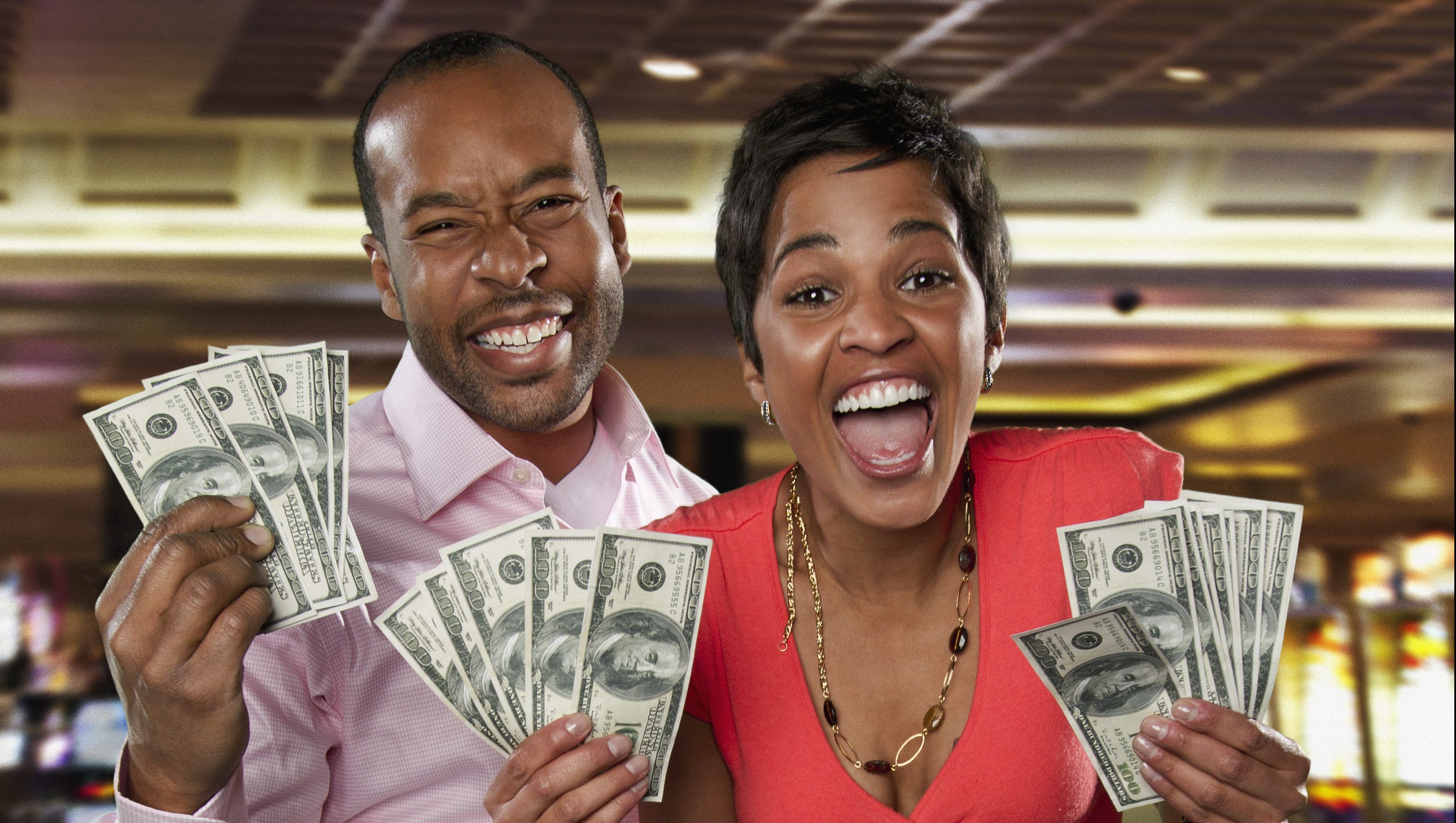 Excited couple holding cash winnings in casino