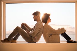 African American couple sitting back to back on a window sill while having relationship difficulties.