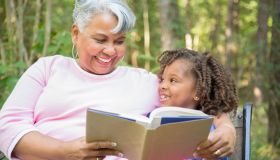 Grandmother and grandchild reading books outdoors together.