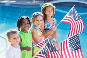 Multi-ethnic children at pool holding American flags
