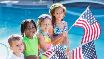 Multi-ethnic children at pool holding American flags