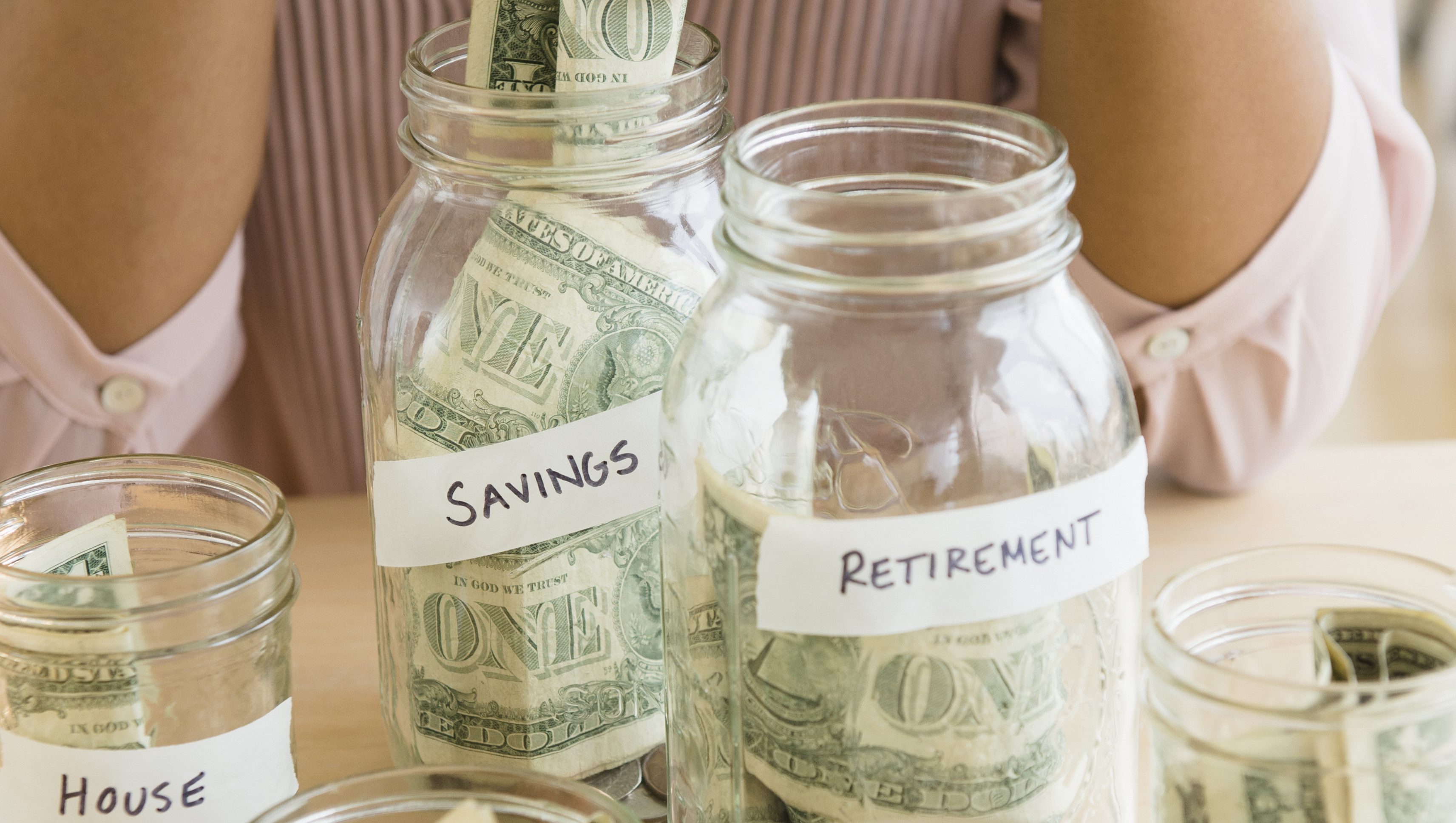 Mixed race woman putting money in savings jars