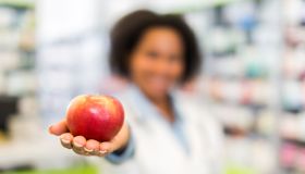 African American pharmacist holding apple in a pharmacy.
