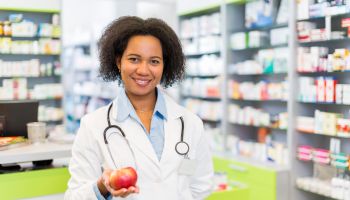 African American pharmacist holding apple and looking at camera.