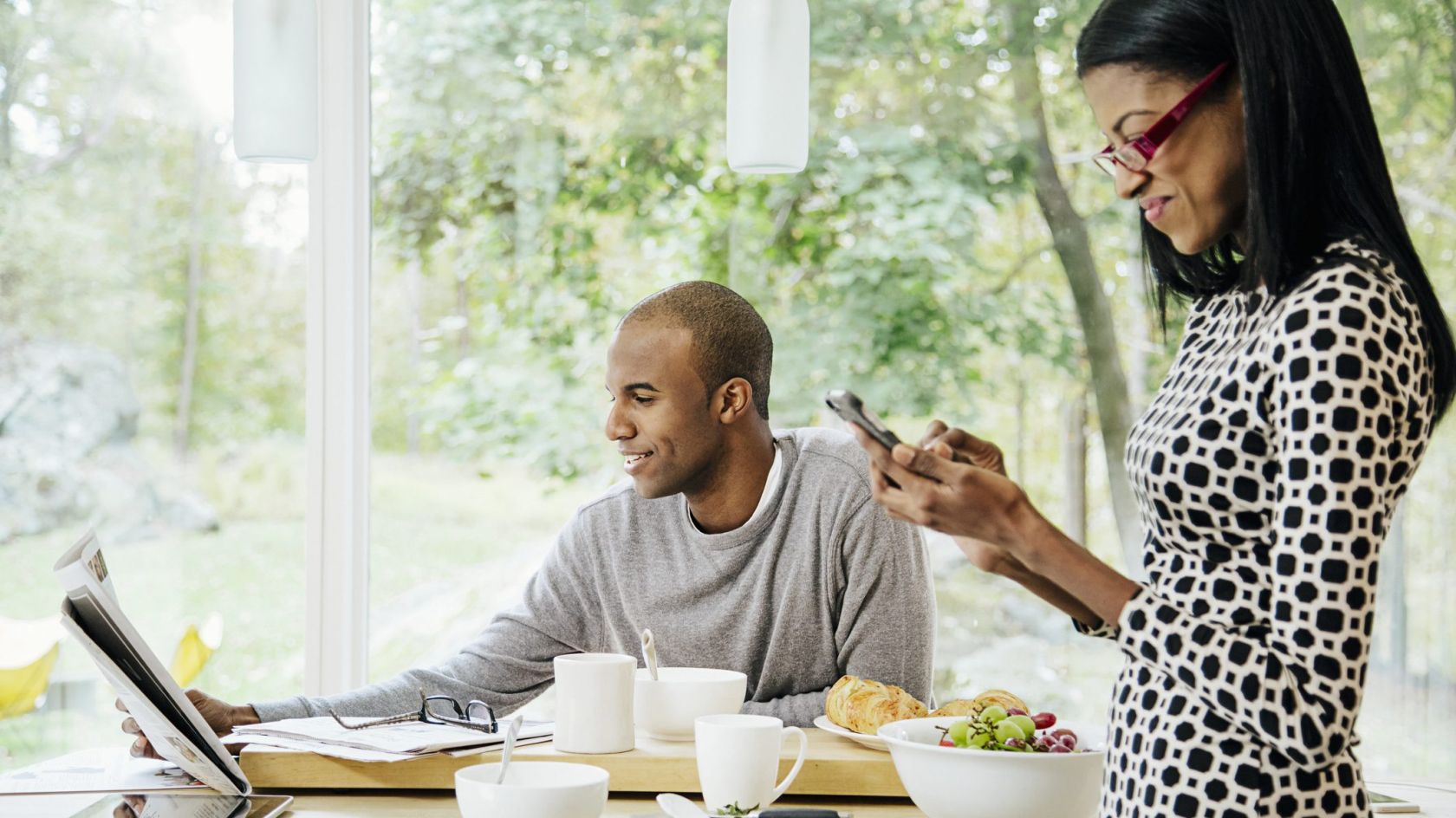 Mid-adult heterosexual couple eating breakfast, Reading newspaper and text messaging