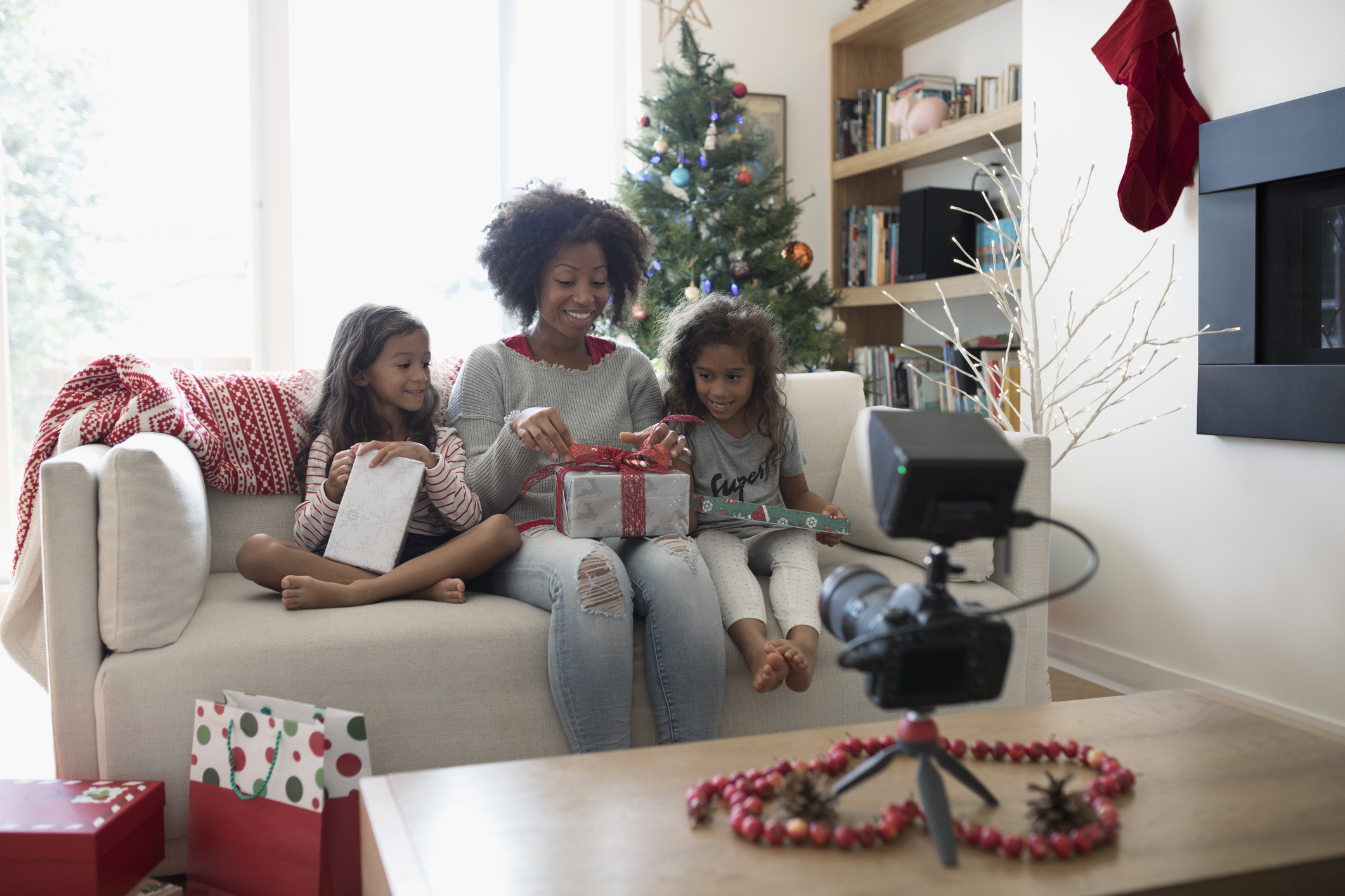 Mother and daughters opening Christmas gifts for video camera in living room