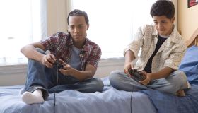 Two teenage boys (16-17) playing video games on bed