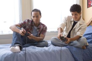 Two teenage boys (16-17) playing video games on bed