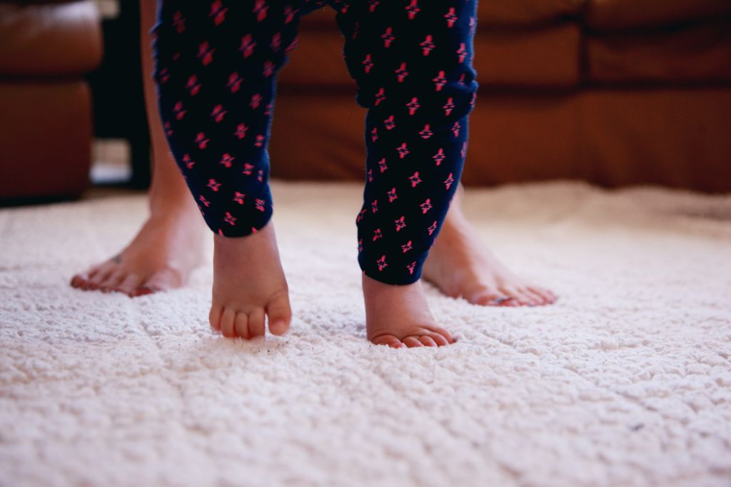 Low Section Of Mother And Baby Girl Walking On Rug At Home