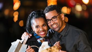 Happy black couple opening a gift bag outdoors at night
