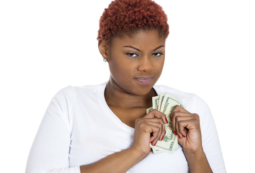 Closeup portrait of grumpy greedy miserly young woman, protecting money, holding dollar bills in hands, looking anxiously with suspicion, isolated white background. Negative human emotions expressions