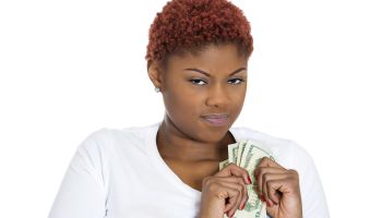 Closeup portrait of grumpy greedy miserly young woman, protecting money, holding dollar bills in hands, looking anxiously with suspicion, isolated white background. Negative human emotions expressions