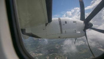 View of Clouds, Land, Sea, Jet Engine and Propeller (with Rolling Shutter) Through Airplane Window