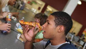 High school student eating pizza in school cafeteria