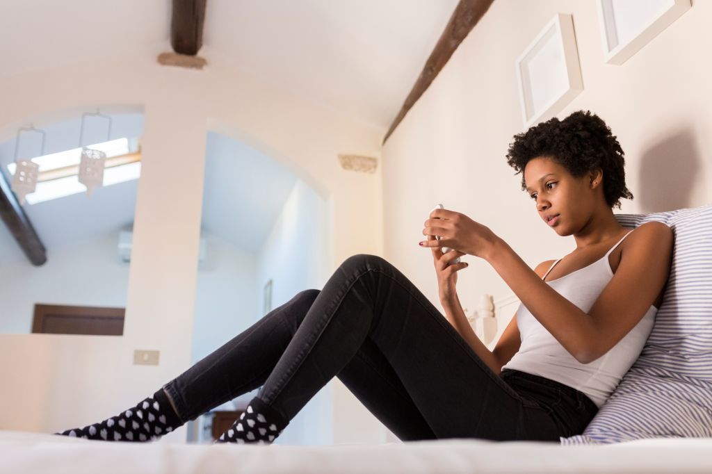 Young woman using cell phone in bedroom