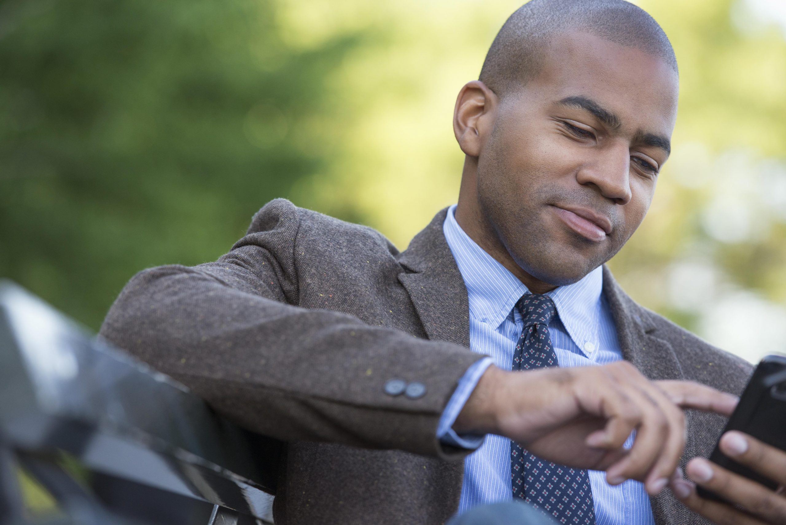 Business people in the city. Keeping in touch on the move. A man seated on a bench. Checking his cell phone.