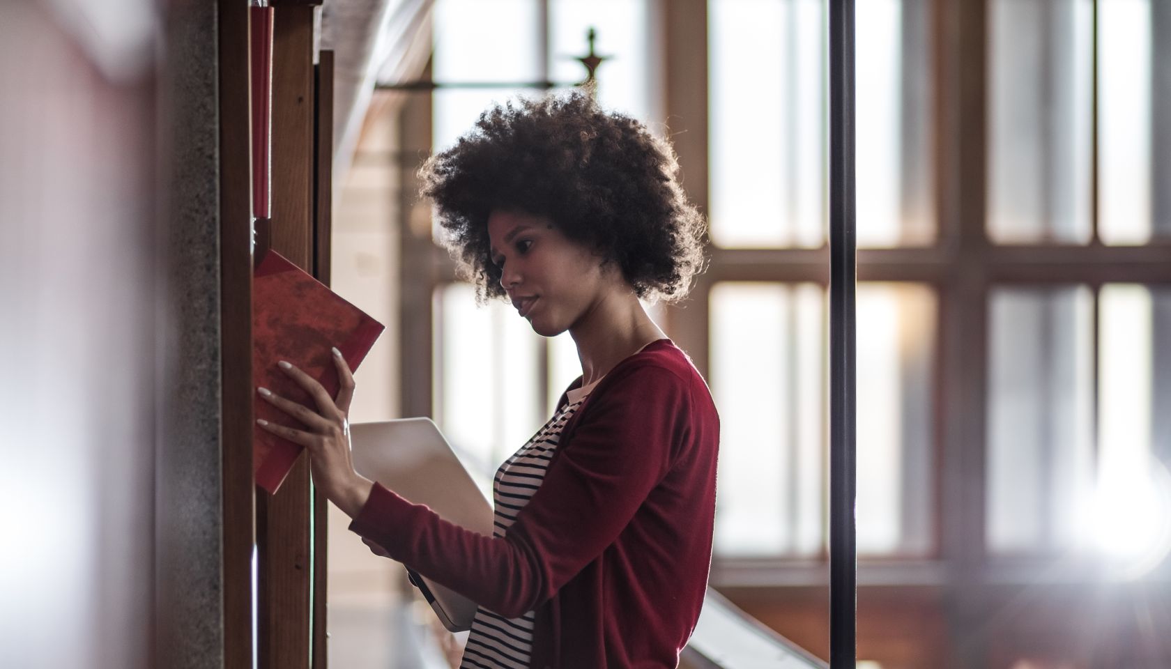 Young Woman in the Library Standing Beside The BookShelf and Studying