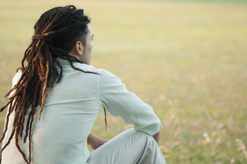 Man with dreadlocks sitting outdoors, rear view