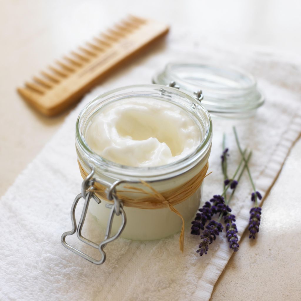 Lavender and rosemary conditioner in a jar, lavender flowers and a comb nearby