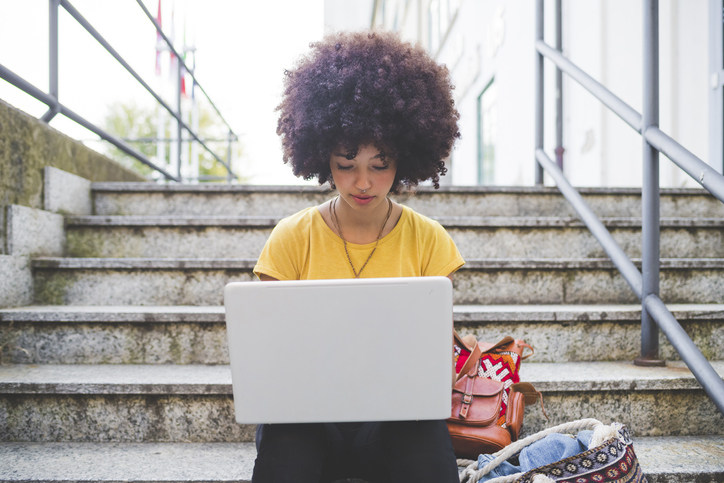 Young woman with afro hairdo using laptop on stairs in the city