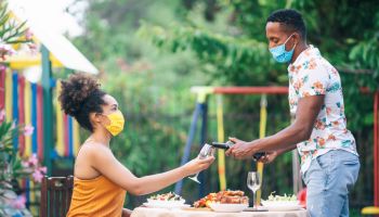 Afro Couple wearing protective face mask having staycation romantic dinner on back yard, during COVID-19