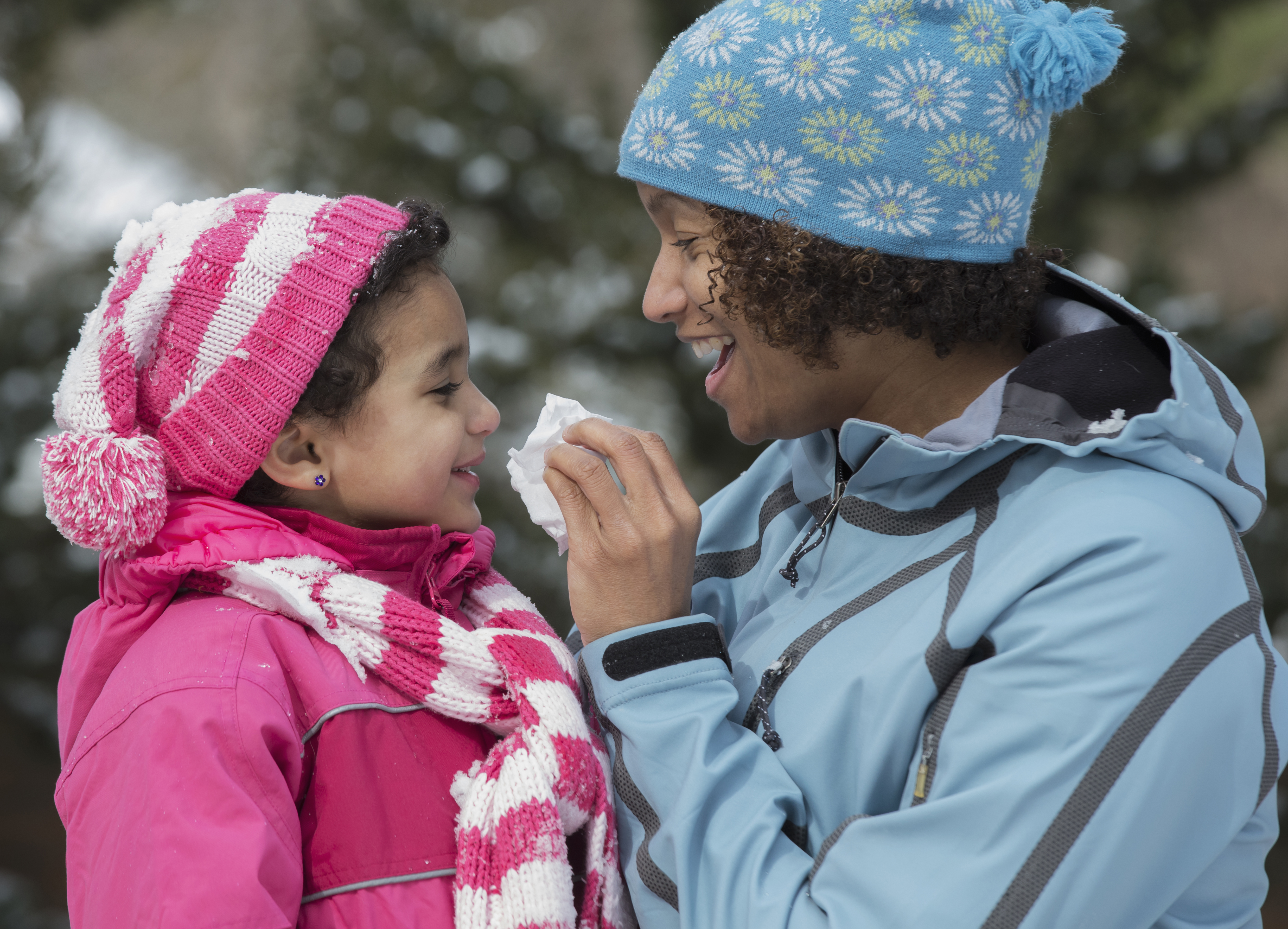 Mother wiping daughter's nose in snow outdoors