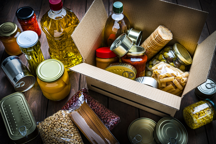 Cardboard box filled with non-perishable foods on wooden table. High angle view.