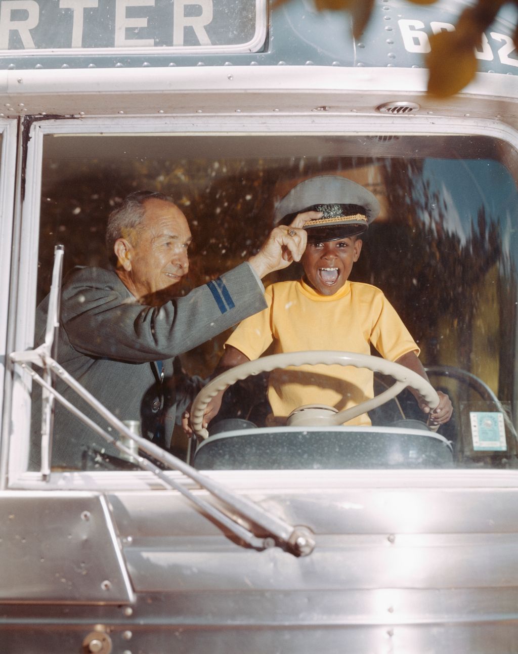 Bus driver giving hat to happy boy holding steering wheel
