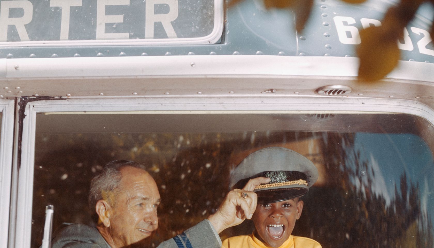 Bus driver giving hat to happy boy holding steering wheel