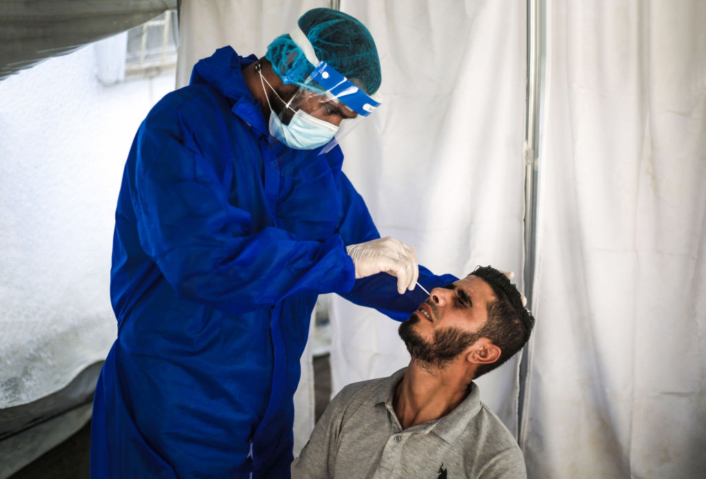 A health worker collects a specimen from a man through a...