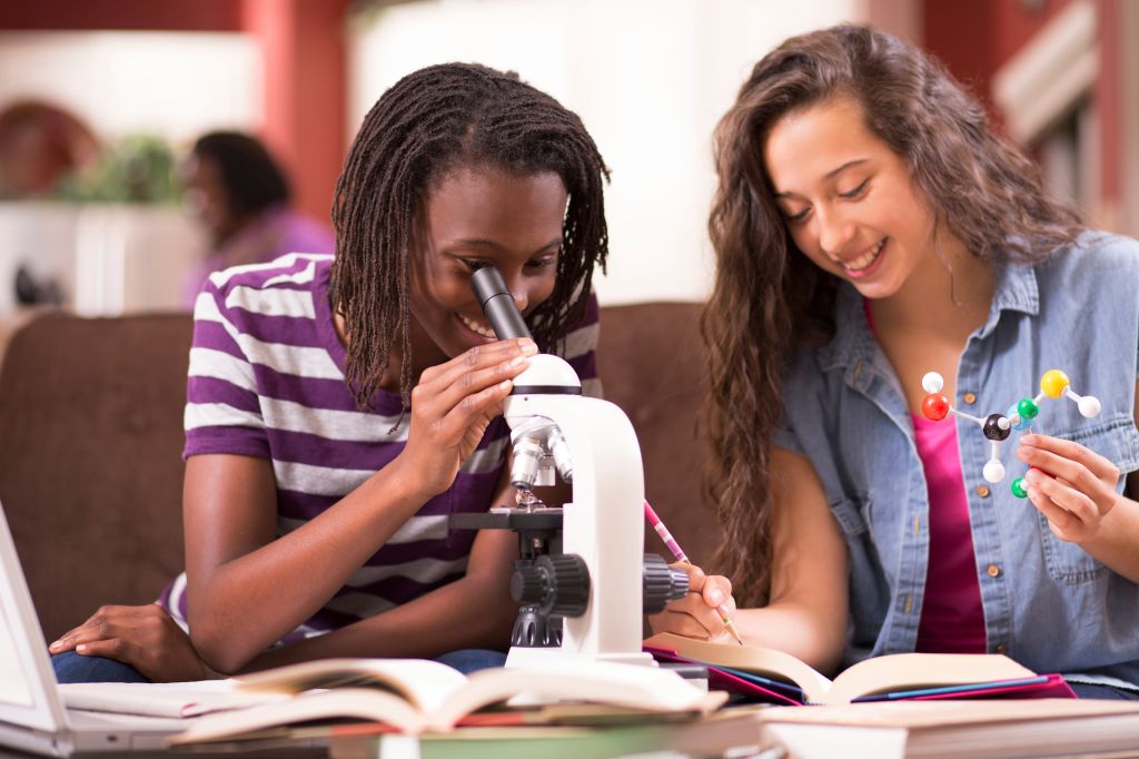 Teenage girls studying science at home using microscope.