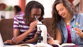 Teenage girls studying science at home using microscope.