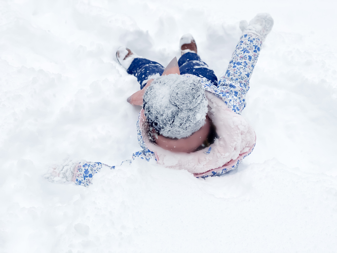 playful mixed-race toddler prepares to make a snow angel in fresh snow after a winter storm