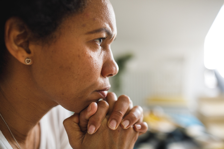 Close up shot of woman sitting with hands clasped under chin, contemplating