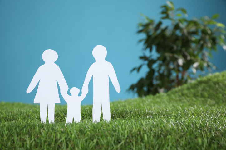 Paper cutout of parents with their child on green grass against light blue background, space for text. Family Day