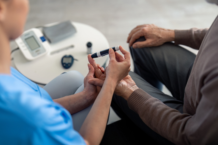 Unrecognizable female nurse checking blood sugar level of senior male patient
