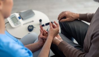 Unrecognizable female nurse checking blood sugar level of senior male patient