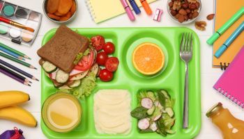 Serving tray of healthy food and stationery on white wooden table, flat lay. School lunch