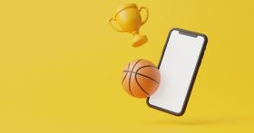 Mobile phone with a white screen, basketball and golden cup are flying on a yellow background with copy space