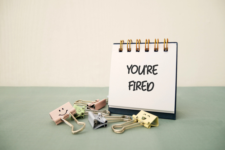 Note on desktop paper saying YOU ARE FIRED on beige background, concept of full time employee being fired, or employer taking decision to let go of low performing staff in corporate company