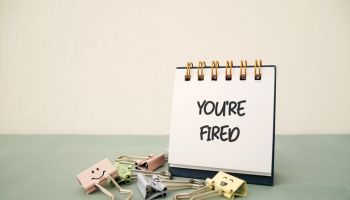 Note on desktop paper saying YOU ARE FIRED on beige background, concept of full time employee being fired, or employer taking decision to let go of low performing staff in corporate company