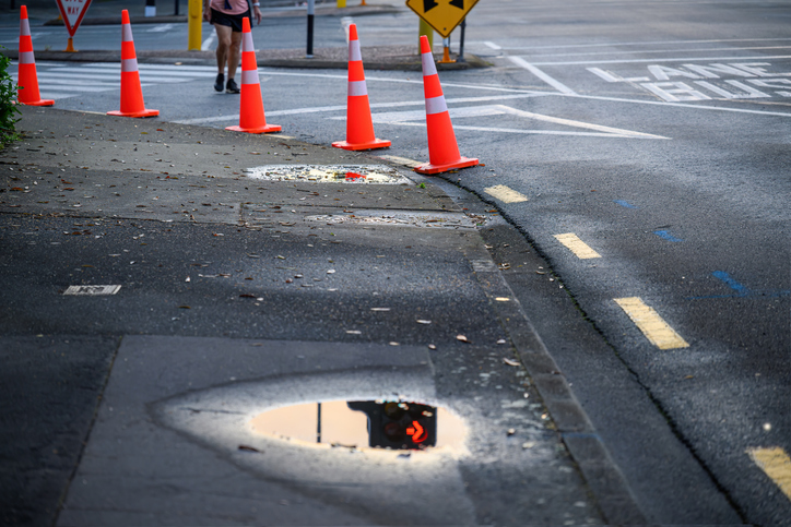 Orange traffic cones lining up the street. Red traffic arrow sign reflected in the puddle of rainwater. Roadworks in Auckland.