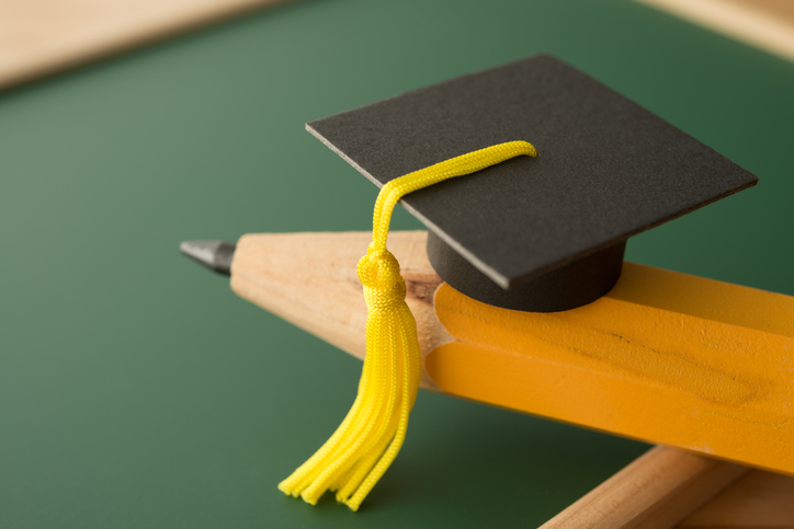 Small graduation cap on pencil with chalkboard background in classroom.