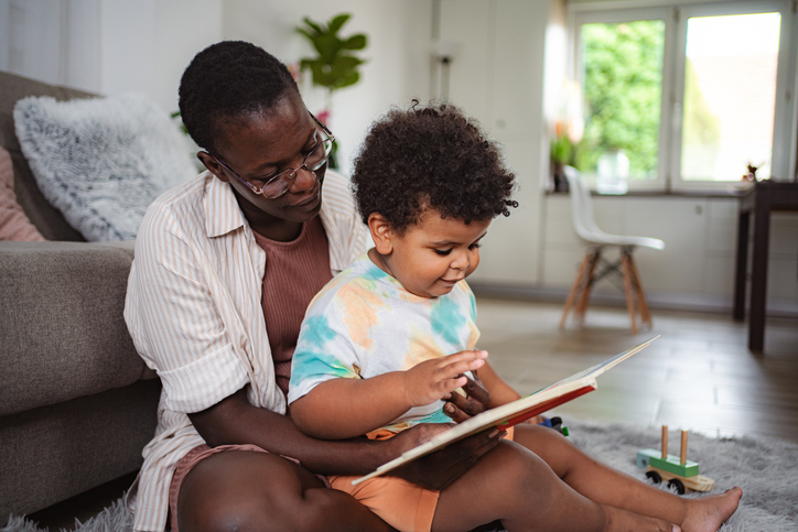 Black mother reading book with toddler son at home