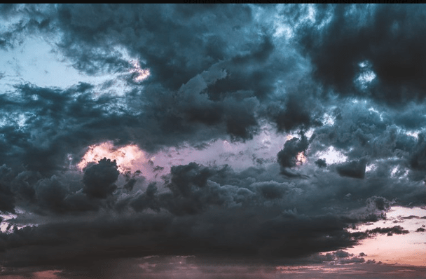 Dramatic stormy sky with dark clouds and patches of pink and orange sunset light.