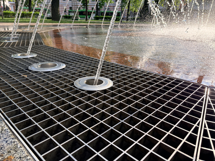 Hot summer. Water in the fountain. A close-up, low-angle view of a modern urban ground fountain or splash pad on a sunny day.