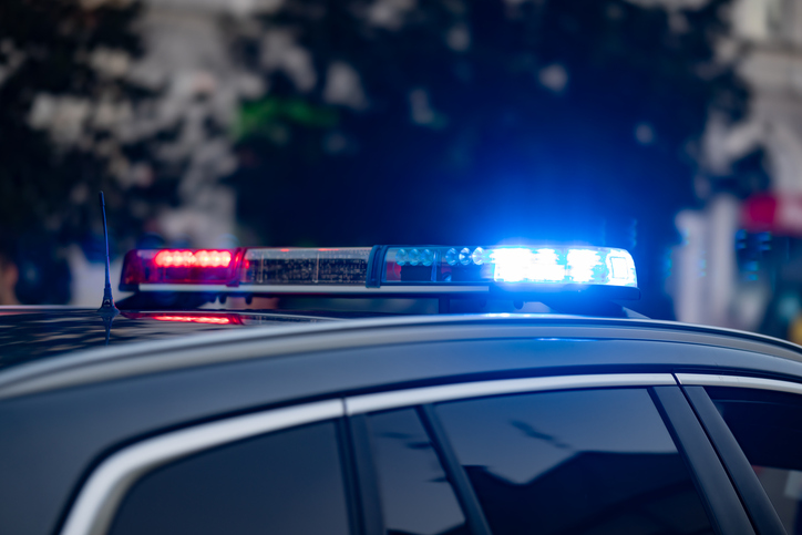 A detailed shot displays the roof of a police car with active blue and red emergency light bars during an intervention in the city. The modern vehicle stands in the streets, while the blurred background with buildings and trees adds dynamic atmosphere.